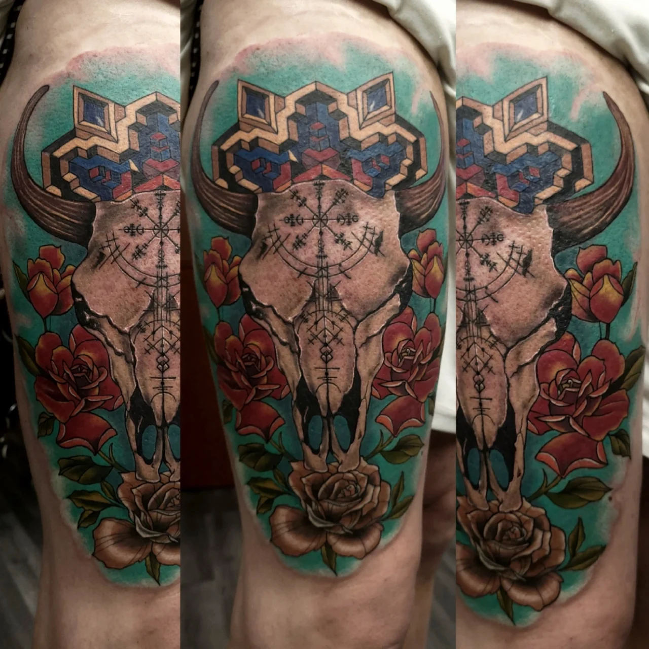 Colorful tattoo of a bull skull with geometric designs above it, surrounded by red and beige roses and green leaves, set against a turquoise background on a persons skin.