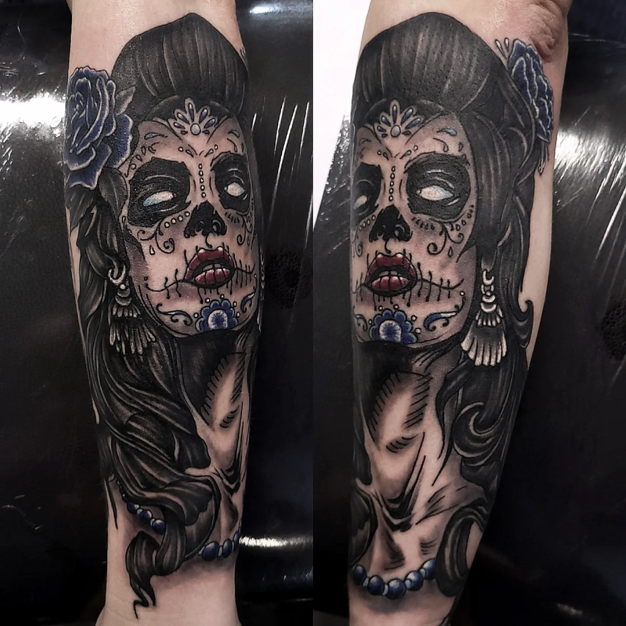 Tattoo of a woman’s face in sugar skull makeup with dark hair, blue floral accents, and jewelry; inspired by Día de los Muertos, on a person’s forearm. The design features detailed shading and vibrant colors.