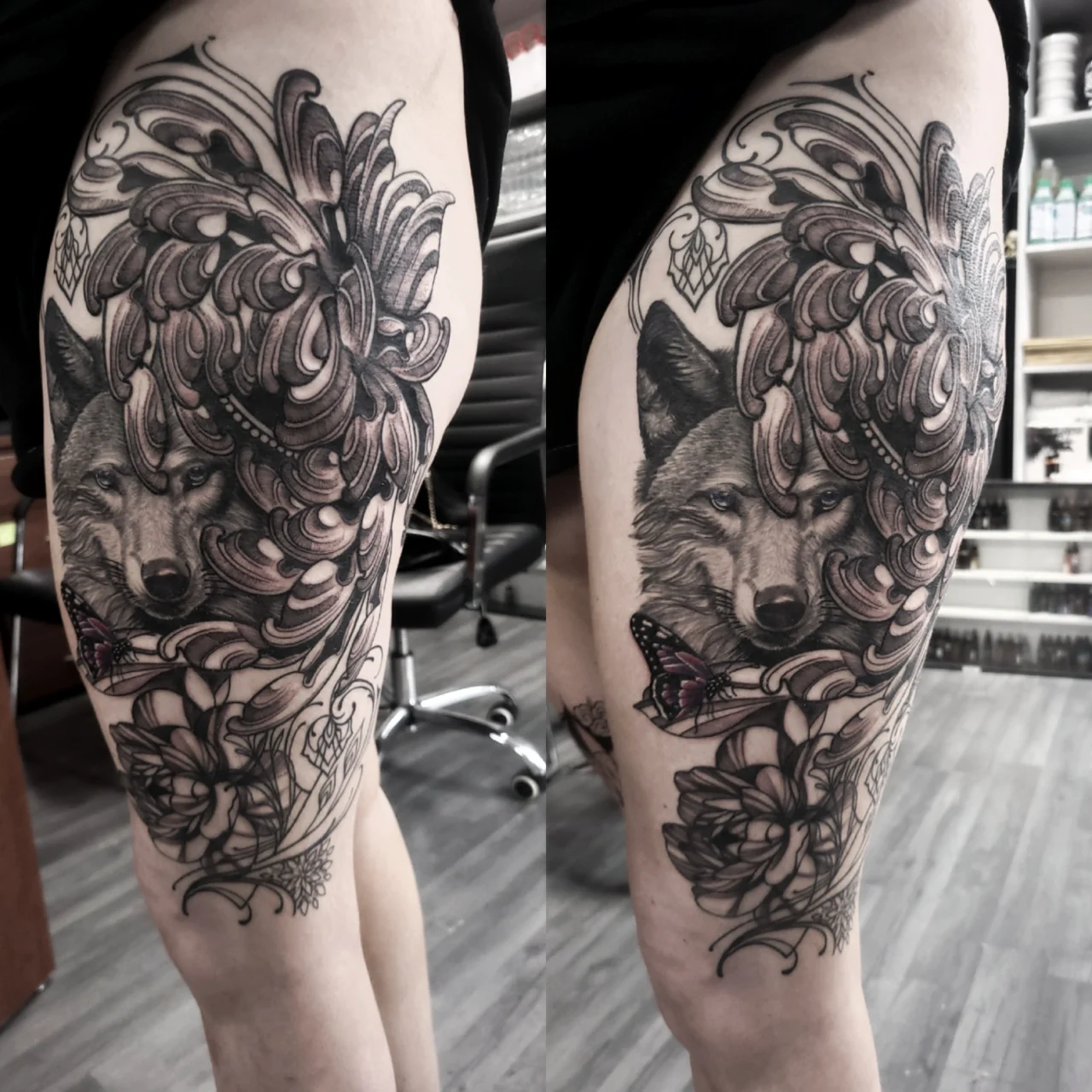 A detailed black and grey thigh tattoo featuring a realistic wolfs face surrounded by ornate floral and leaf designs, with a small colored butterfly near the bottom.