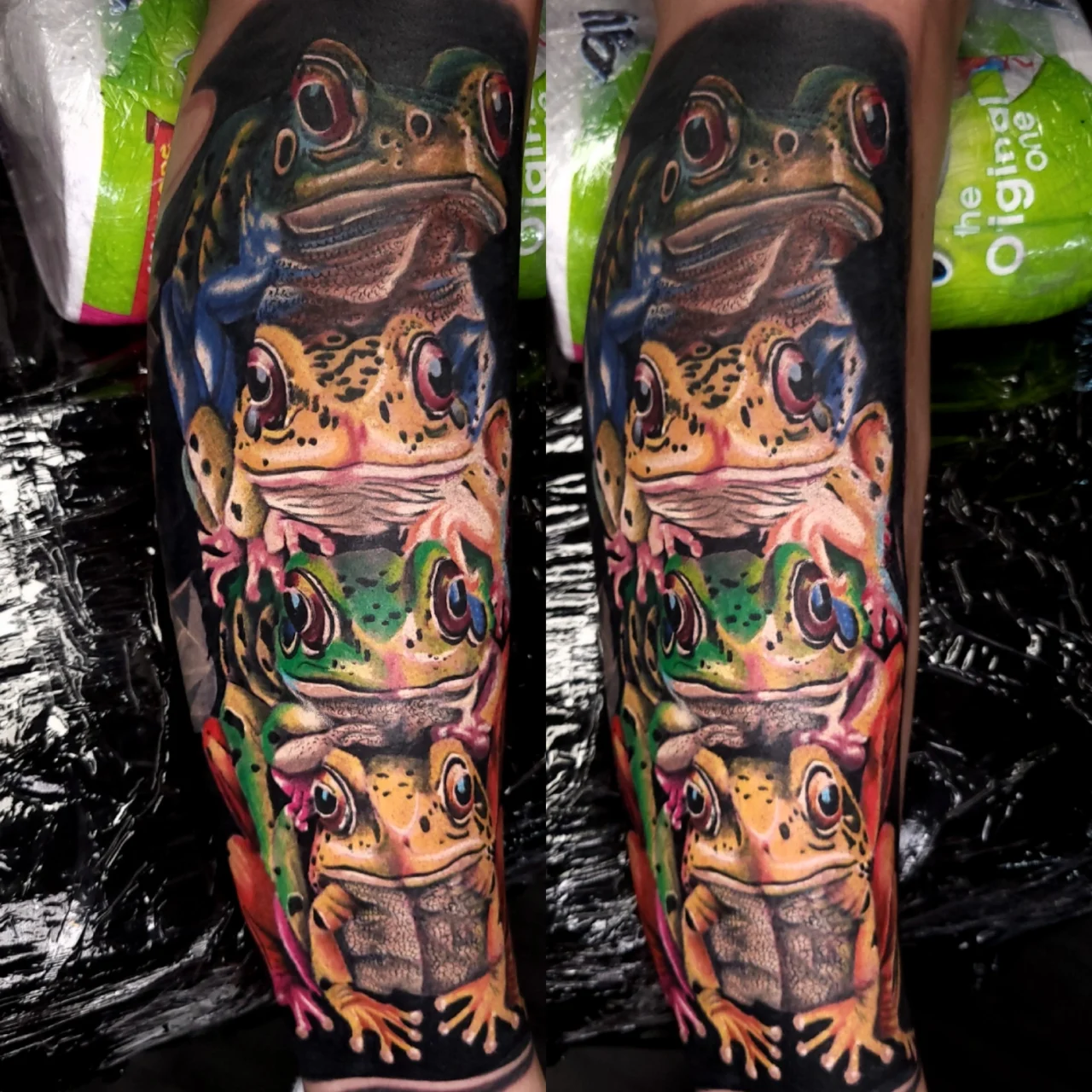 A colorful tattoo on a forearm features four realistic frogs stacked vertically, each with vibrant detailed patterns, against a dark background. The tattoo is vivid and occupies most of the forearm.