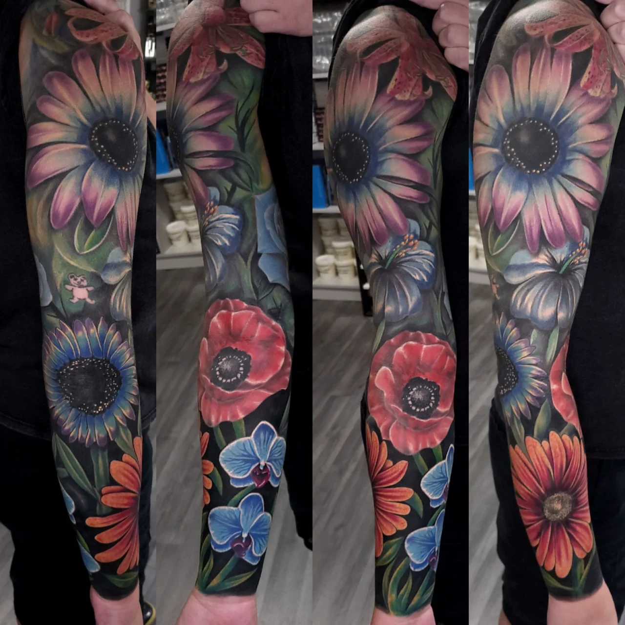 A colorful full-sleeve tattoo featuring large, detailed flowers in vibrant shades of pink, purple, blue, red, and orange, covering the entire arm from shoulder to wrist.