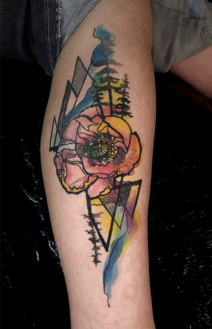 A tattoo on a calf featuring a large, colorful flower with watercolor splashes, geometric shapes, and silhouettes of pine trees. The design combines vibrant hues and bold black outlines for a striking effect.