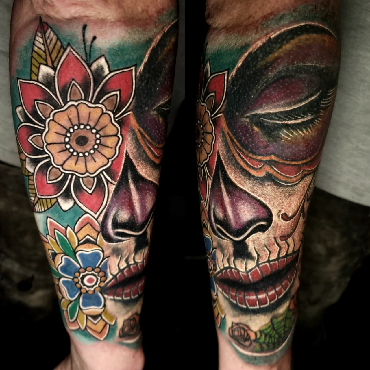 Colorful tattoo on a forearm featuring a Day of the Dead sugar skull face with vibrant flowers, intricate patterns, and bold shading, covering most of the skin.