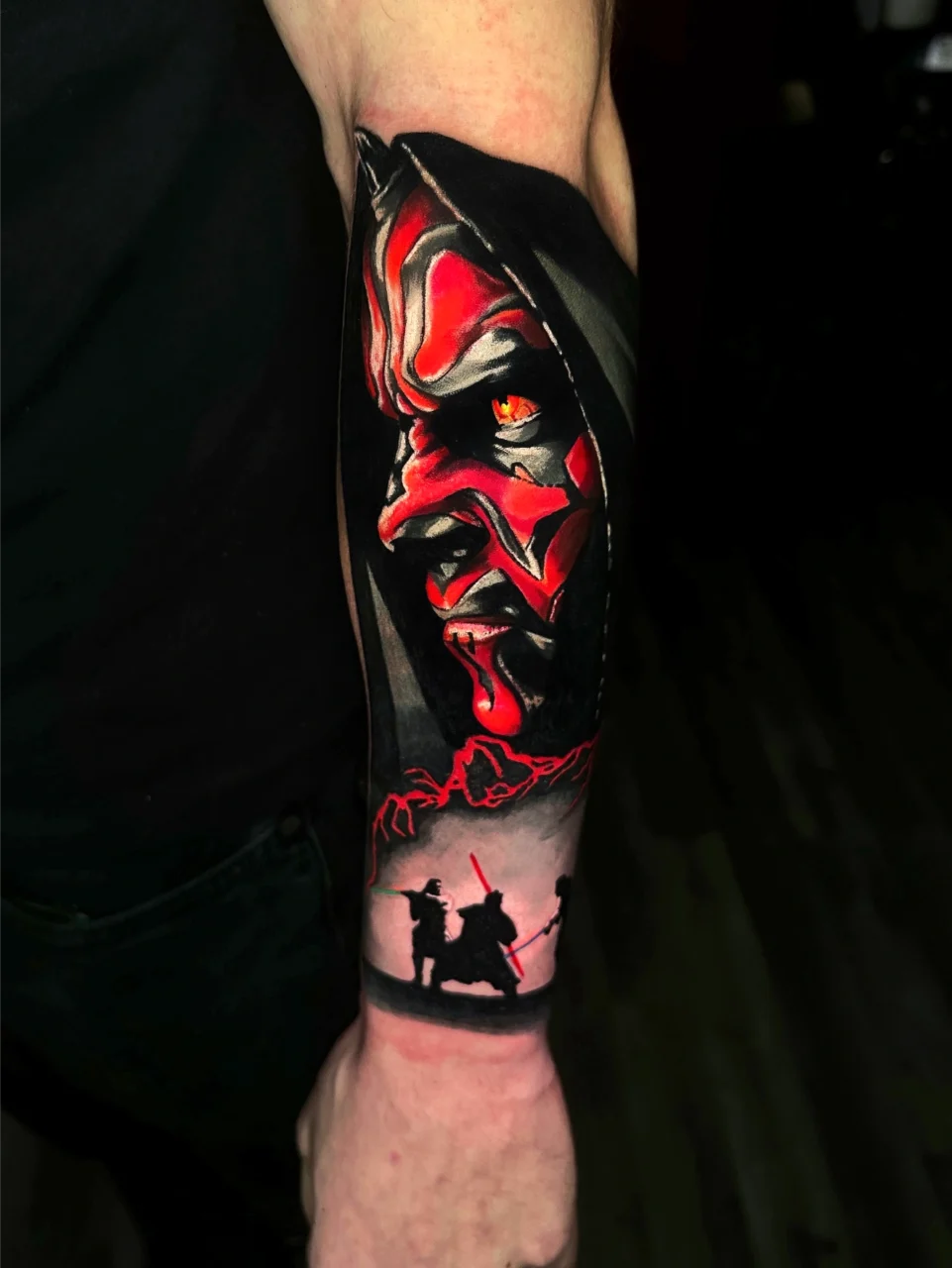 A tattoo on a forearm features a vivid, red-faced horned figure with yellow eyes in a hood, above black silhouettes of three characters holding lightsabers in a duel scene.