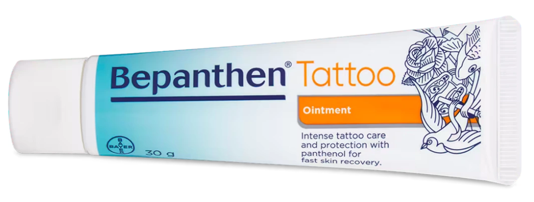 A 30g tube of Bepanthen Tattoo Ointment, with blue and orange text and tattoo-inspired line art, designed for tattoo care and fast skin recovery—perfect after a session at your favorite tattoo studio in Dublin or trying new spider ink.